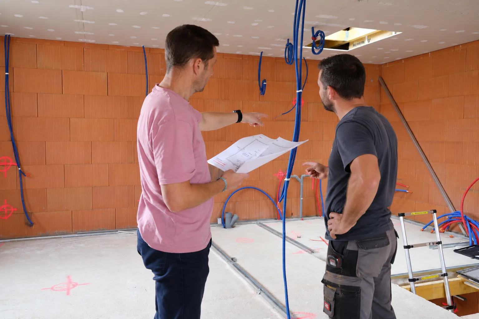 Christophe en visite de chantier, plan en main, montre un point à un artisan